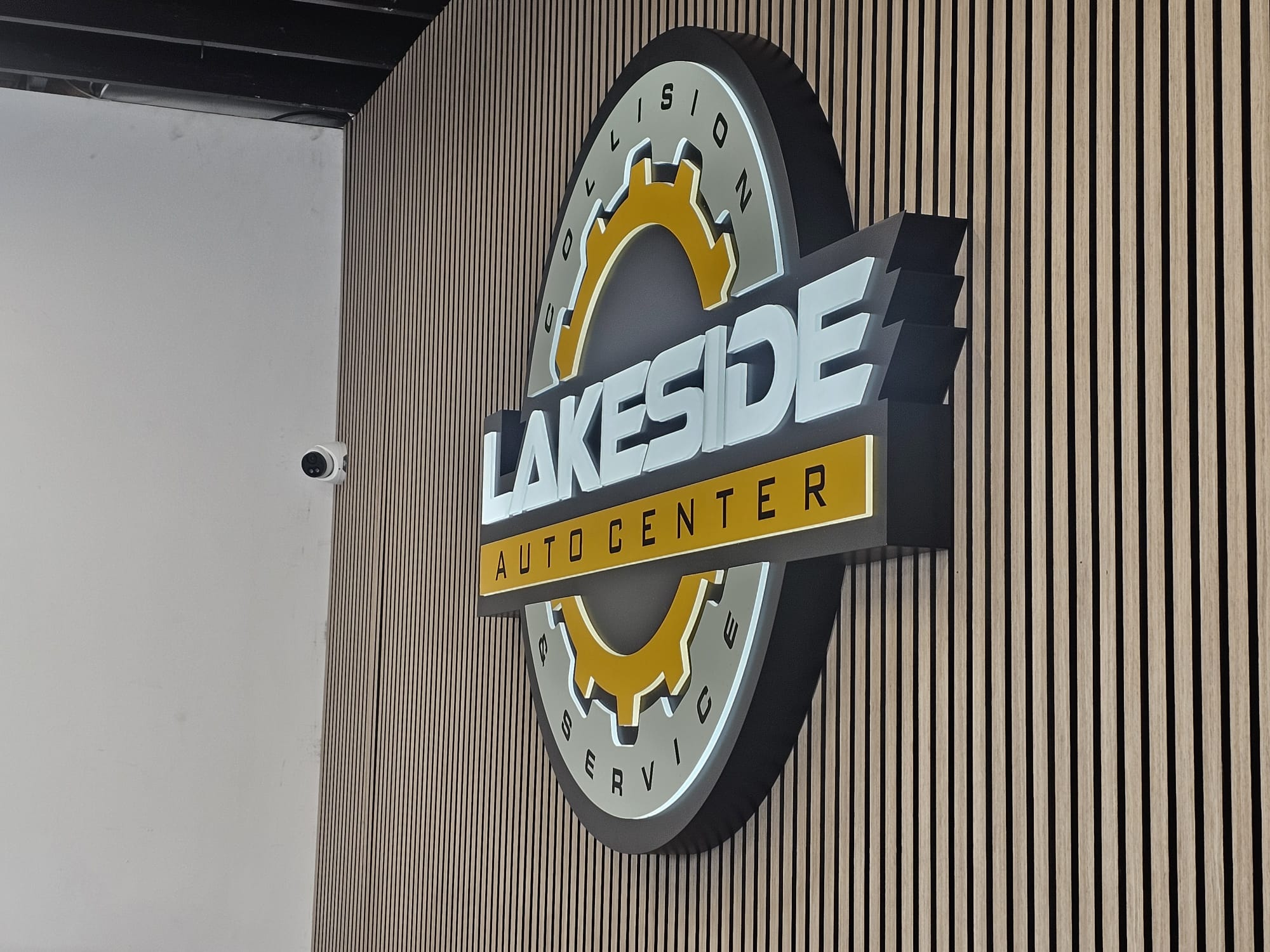 Professional illuminated 3D business sign for an auto center and collision service mounted on a slat wall
