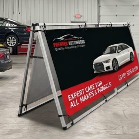 Metal A-frame with an auto repair banner and a car photograph inside a garage.
