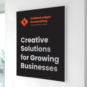 Black and orange foam board sign with business branding mounted on an indoor wall.