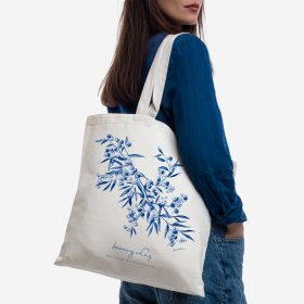 Person carrying a cream tote bag printed with blue floral artwork.