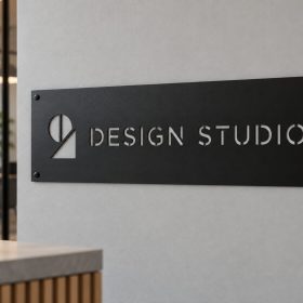 Rectangular black powder coated steel office sign with Design Studio logo cut out, mounted with corner screws